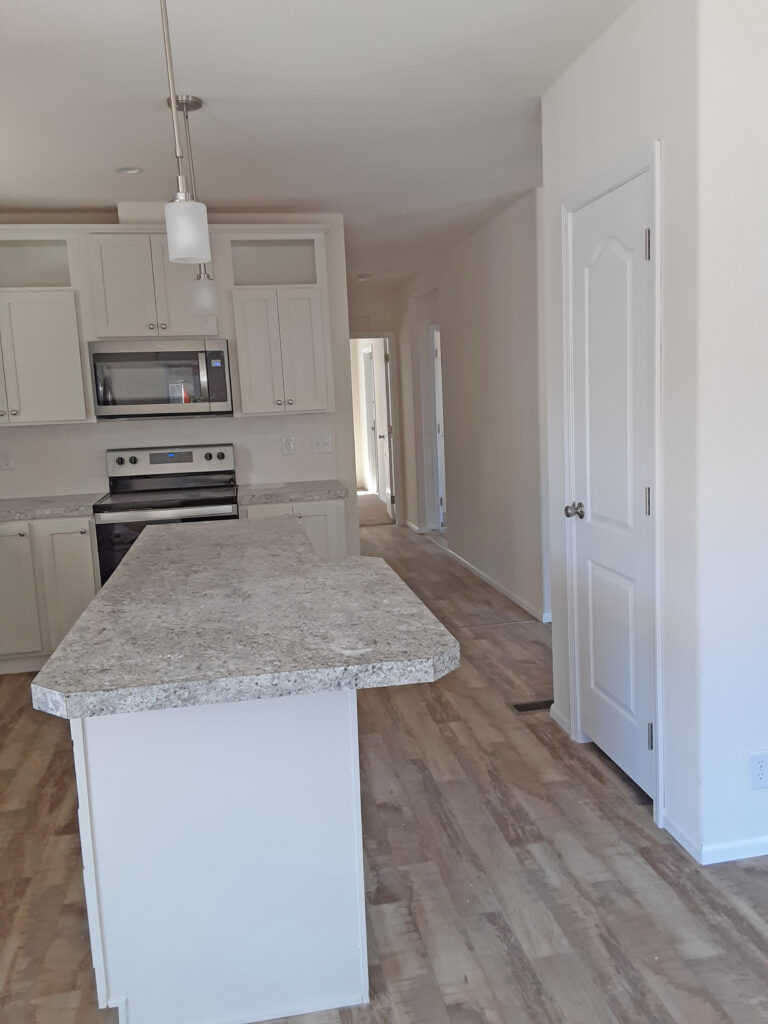 An empty kitchen with white cabinets and hardwood floors.