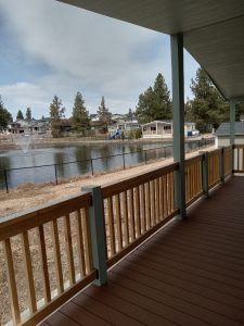 A deck with a fence and a lake in the background showcasing four brand new manufactured homes.