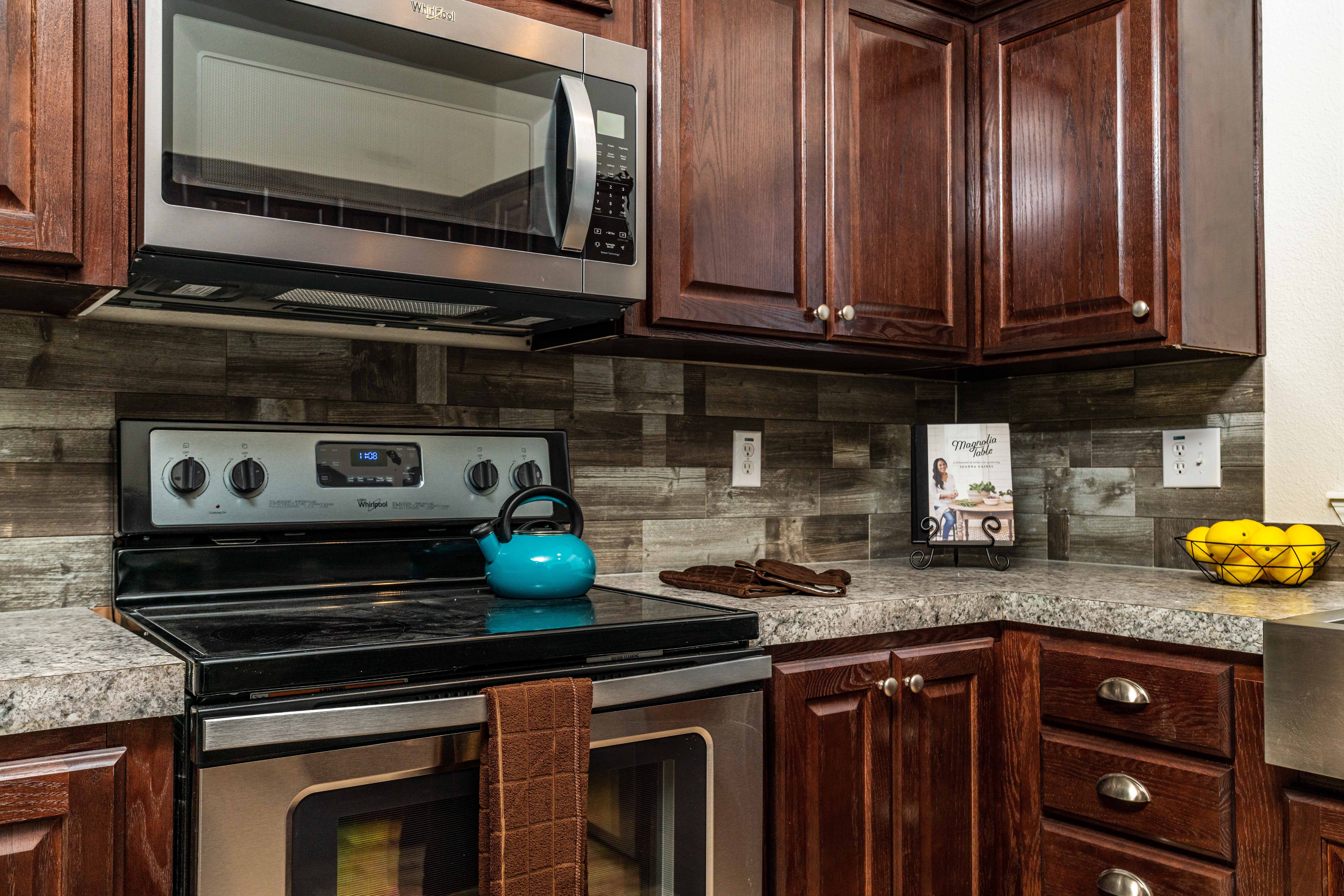 Modern kitchen with dark wood cabinets, stainless steel appliances, a teal kettle on the stove, brown towel, and a bowl of lemons on the counter.