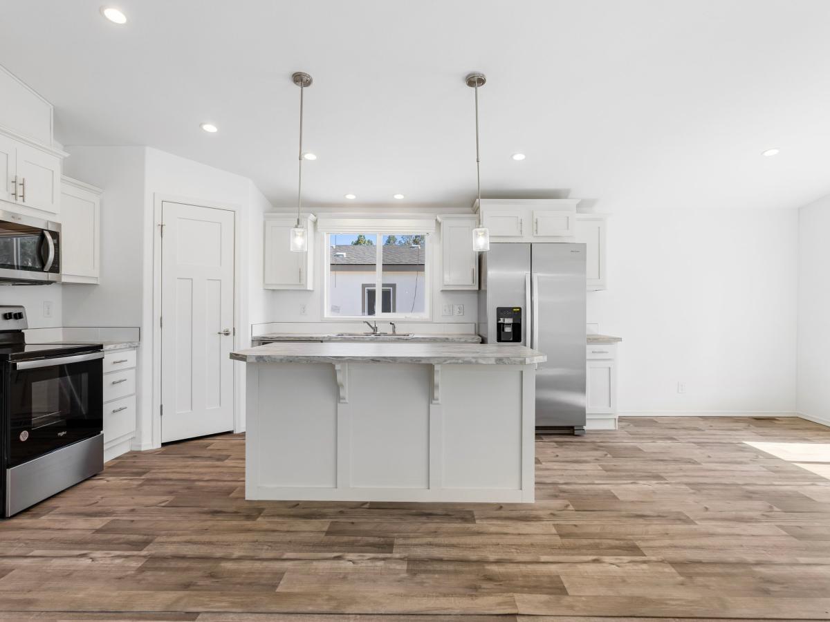 A white kitchen with hardwood floors and stainless steel appliances.