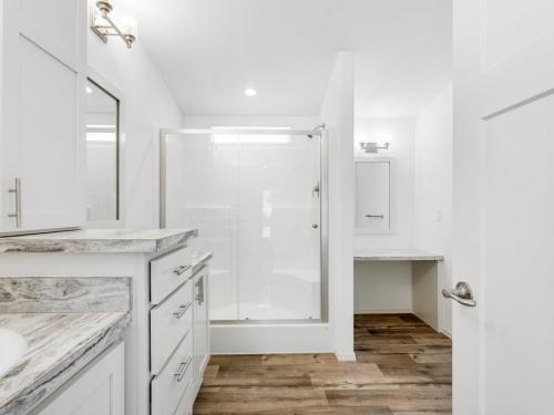 A white bathroom with wood floors and a walk in shower.