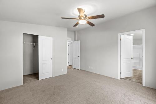An empty bedroom with a ceiling fan and carpet.