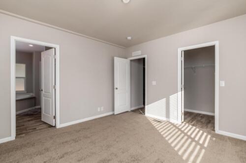 An empty room with closets and tan carpet.