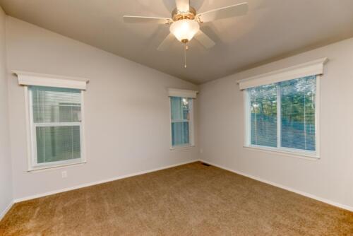 An empty room with two windows and a ceiling fan.